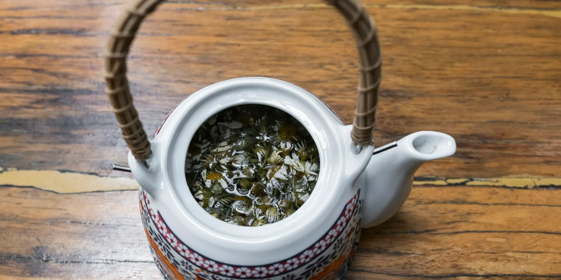 Chamomile flowers steeping in a teapot on a wooden table